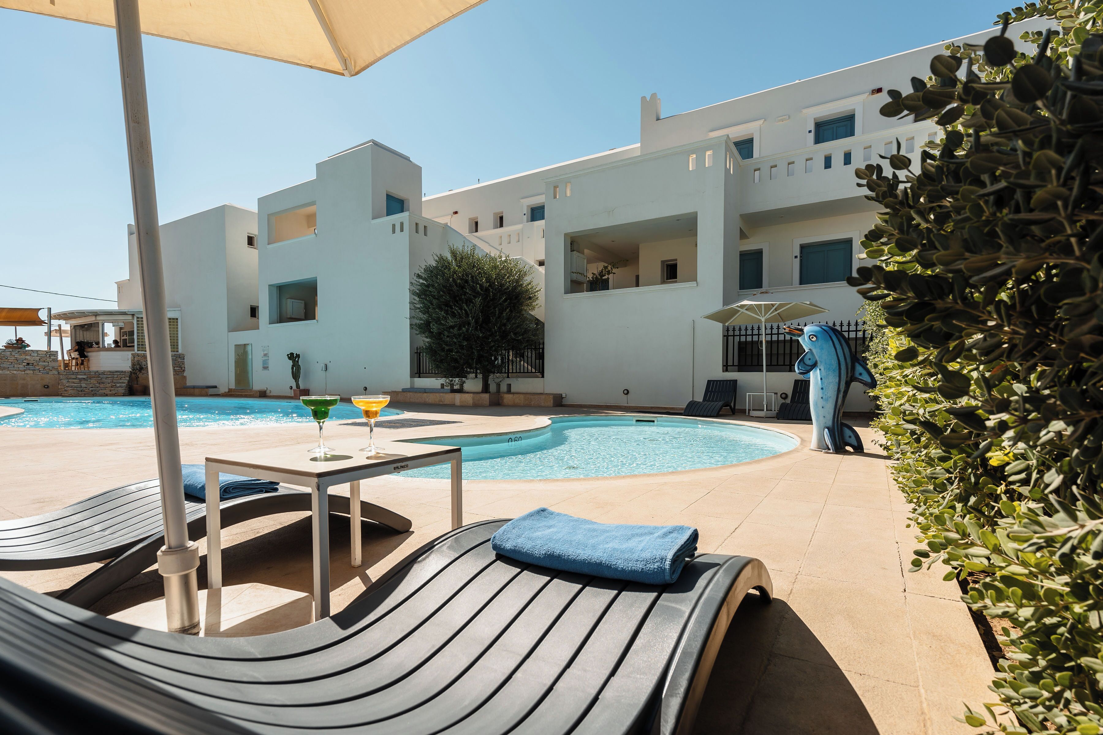 A poolside area with lounge chairs, a table with a drink, and a building in the background.