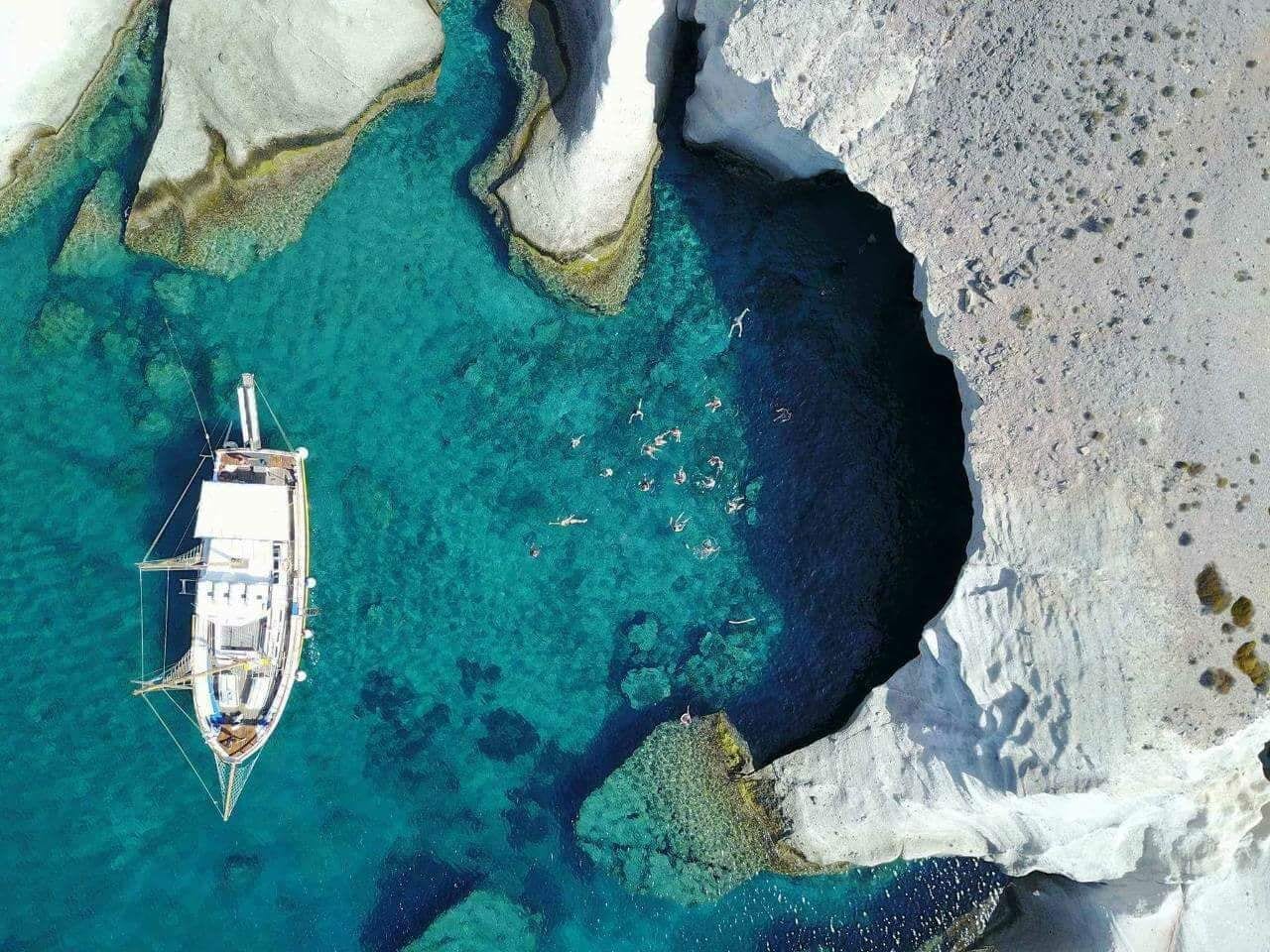 An aerial view of a boat anchored near a rocky coastline with clear turquoise waters.