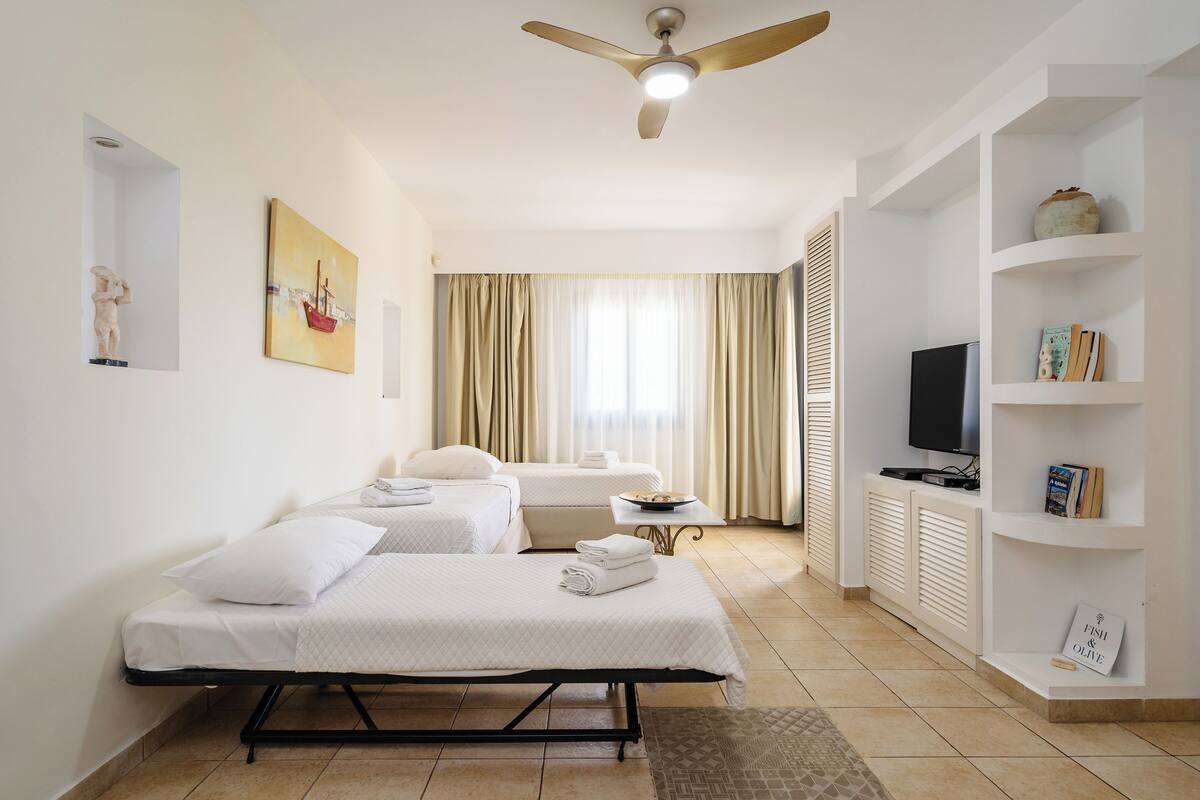 A hotel room with two beds, a ceiling fan, a television, and a bookshelf.