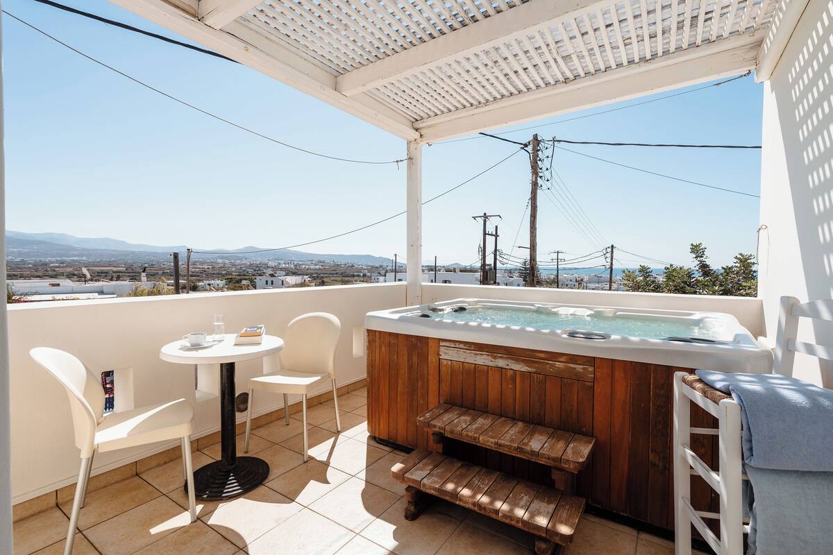 A balcony with a hot tub, white chairs, a small table, and a wooden bench.