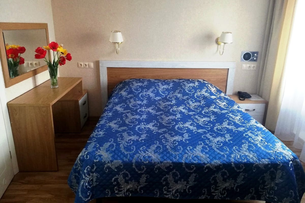 Quarto de hotel com cama, mesas de cabeceira, espelho e um vaso com flores.