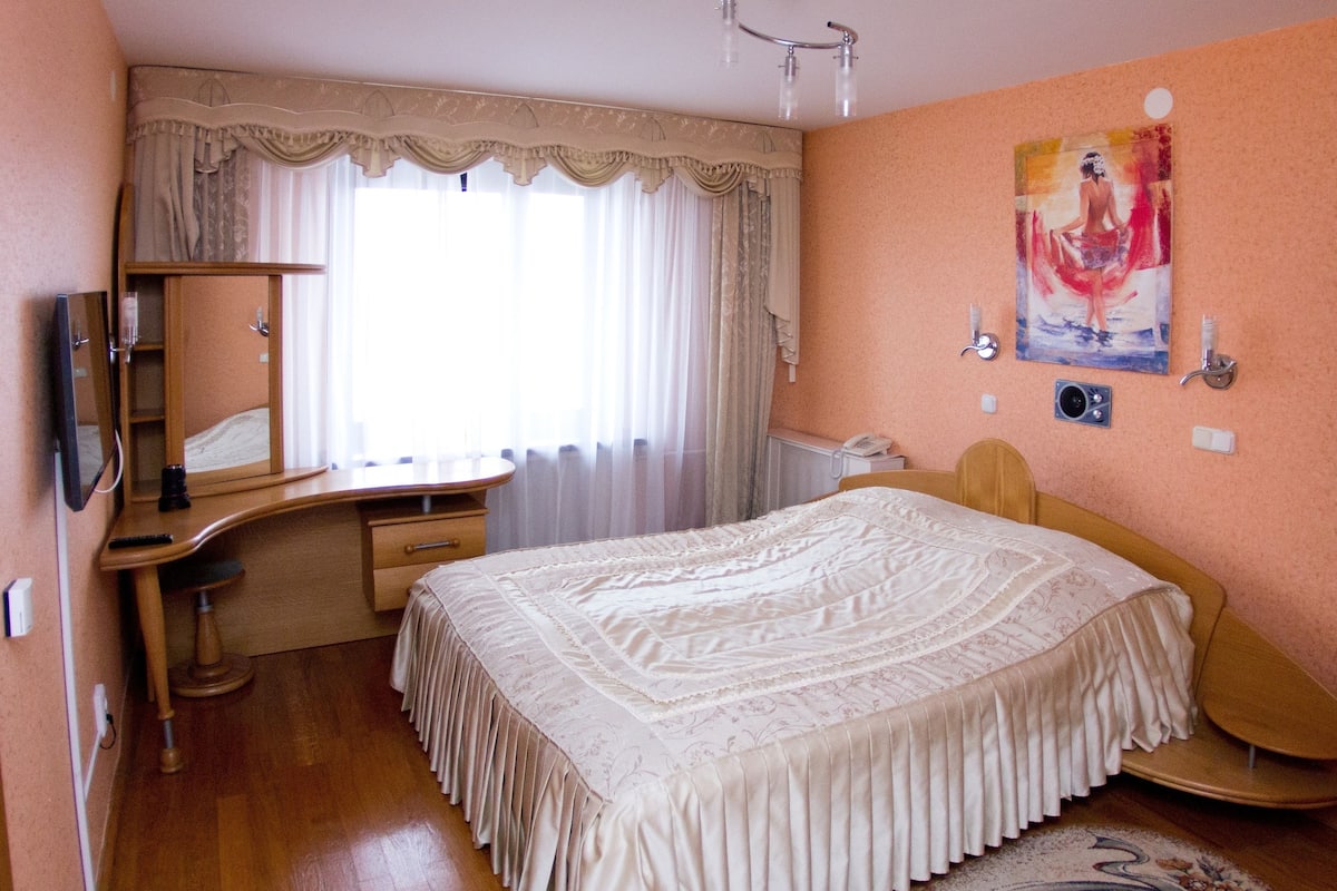 Quarto com uma cama grande, uma escrivaninha de madeira, um espelho, um telefone e um quadro na parede.