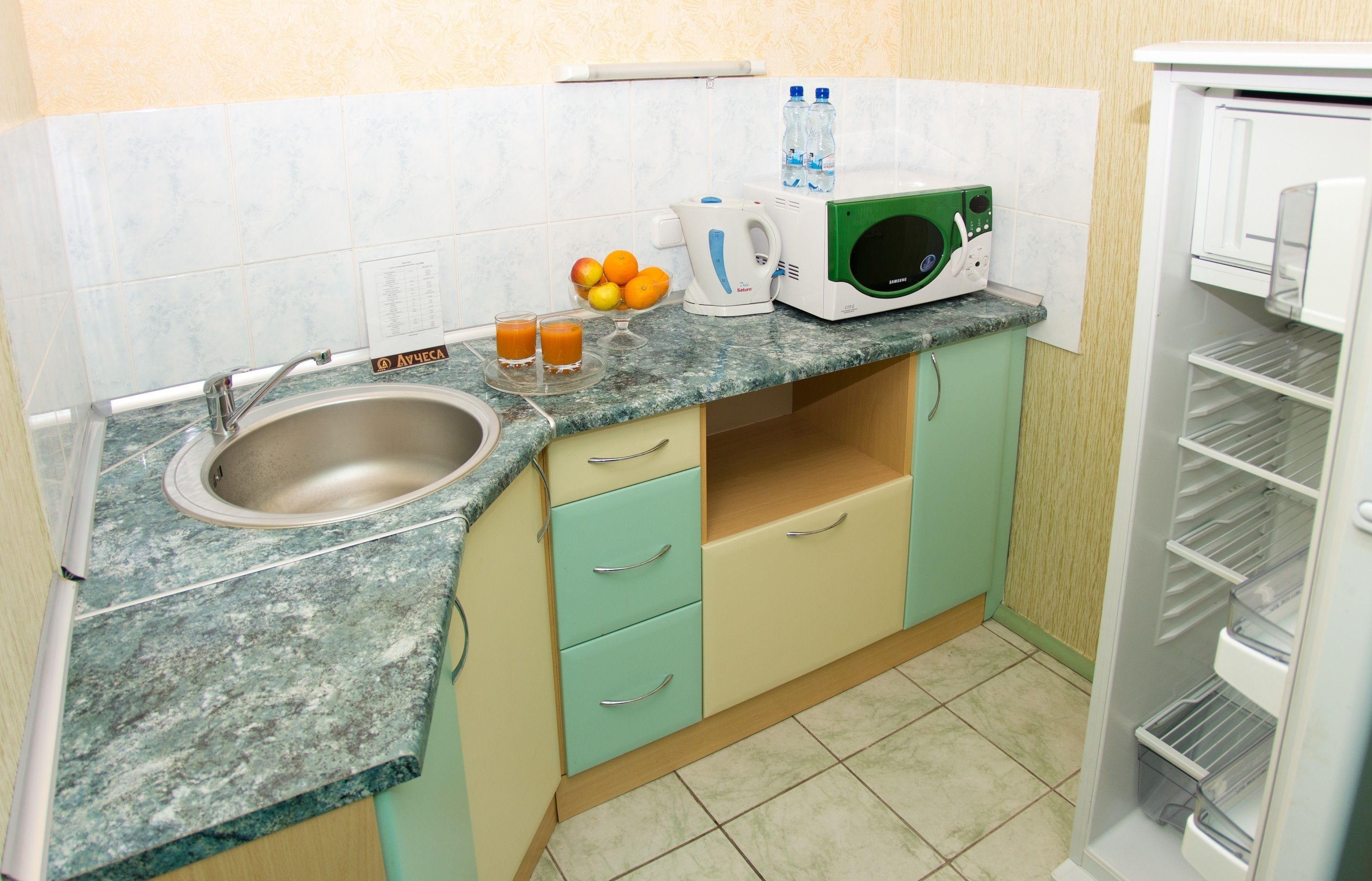 Eine kleine Küche mit Spüle, Mikrowelle, Wasserkocher und Kühlschrank.