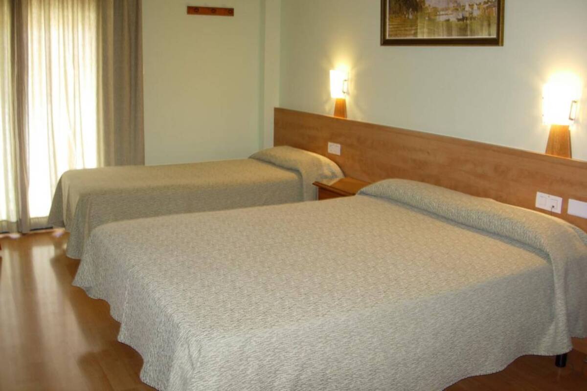 A hotel room with two beds, a wooden headboard, a painting on the wall, and a window with curtains.