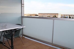 A balcony with a table and chair, a view of buildings in the distance, and a tiled floor. - Hotel Flora Parc (Castelldefels)
