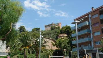 Un edificio con balcón, una palmera y una torre al fondo.
