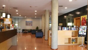 A hotel lobby with a reception desk, seating area, and columns. - Hotel Flora Parc (Castelldefels)
