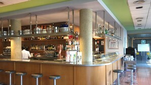 A bar area with stools, shelves stocked with bottles, and a counter. - Hotel Flora Parc (Castelldefels)