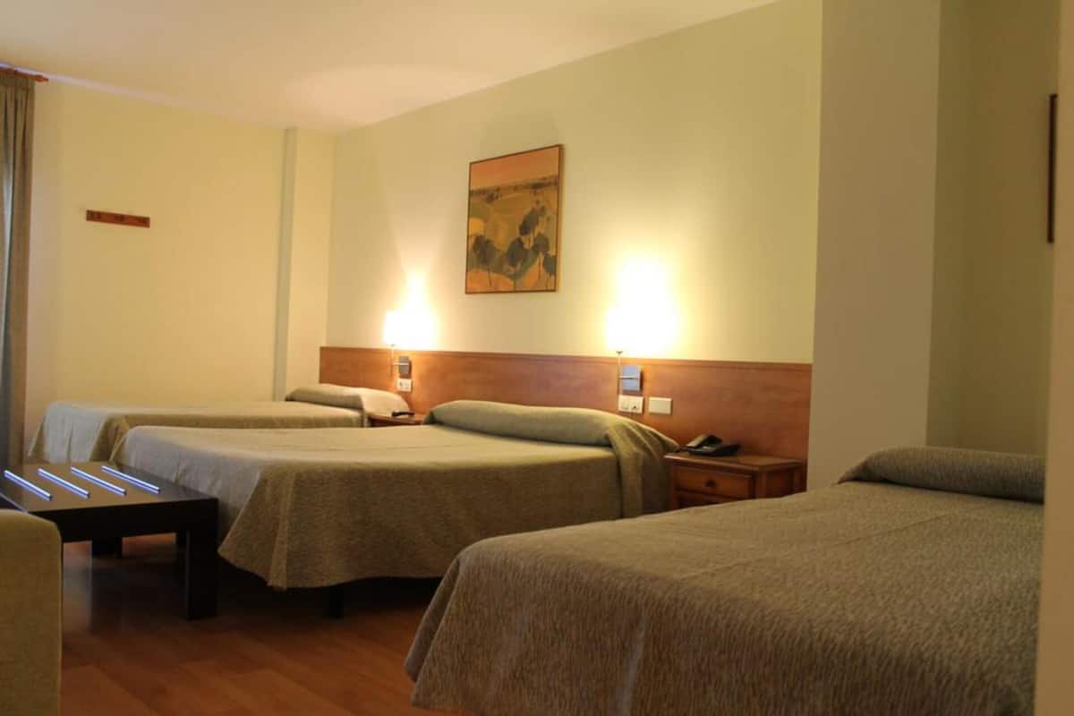 A hotel room with two single beds, a bedside table with a lamp, a wooden headboard, and a painting on the wall.