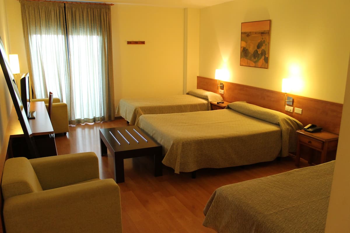 A hotel room with two beds, a desk, a chair, and a lamp.