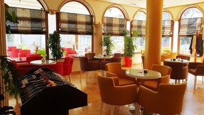 Un hall d’hôtel avec des tables et des chaises rondes, de grandes colonnes et des plantes en pot.