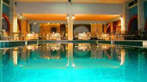 Une grande piscine intérieure dotée d’un plafond miroitant, entourée de tables et de chaises, et comprenant une scène centrale.