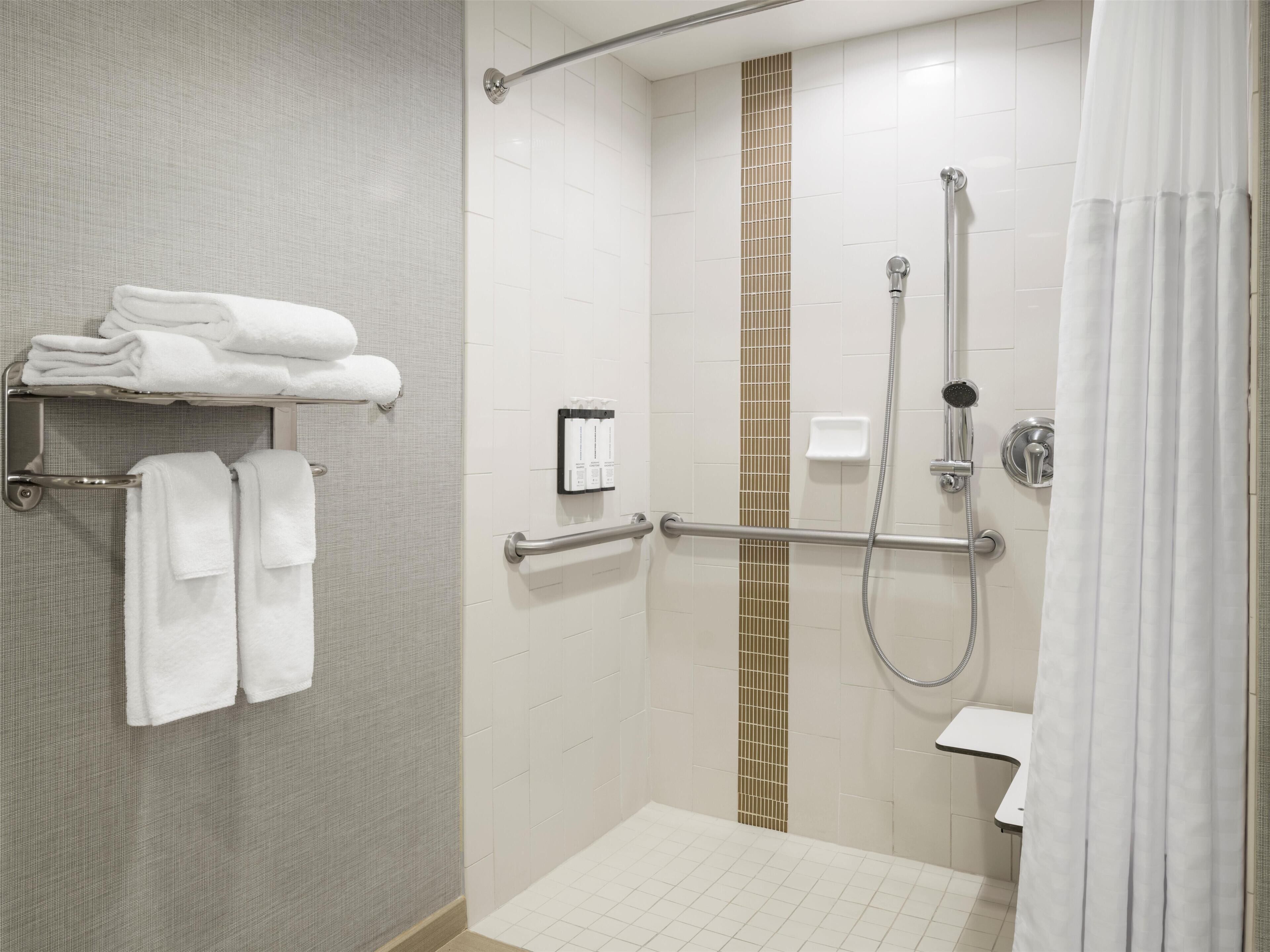 Un baño moderno con ducha a nivel, barras de apoyo, toallero y retrete.