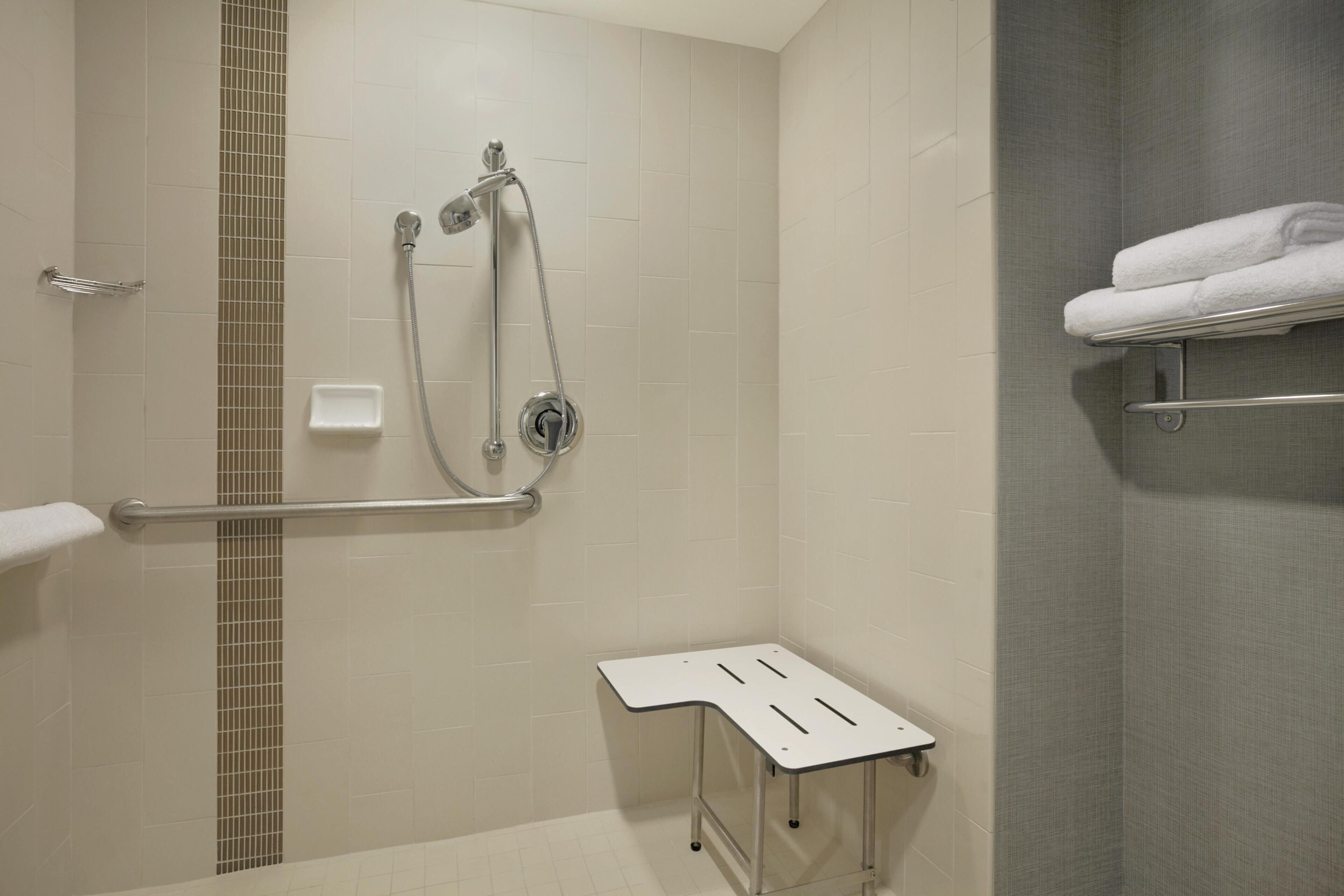 Ein Badezimmer mit Dusche, Haltegriffen, Handtuchhalter und einem kleinen Tisch.