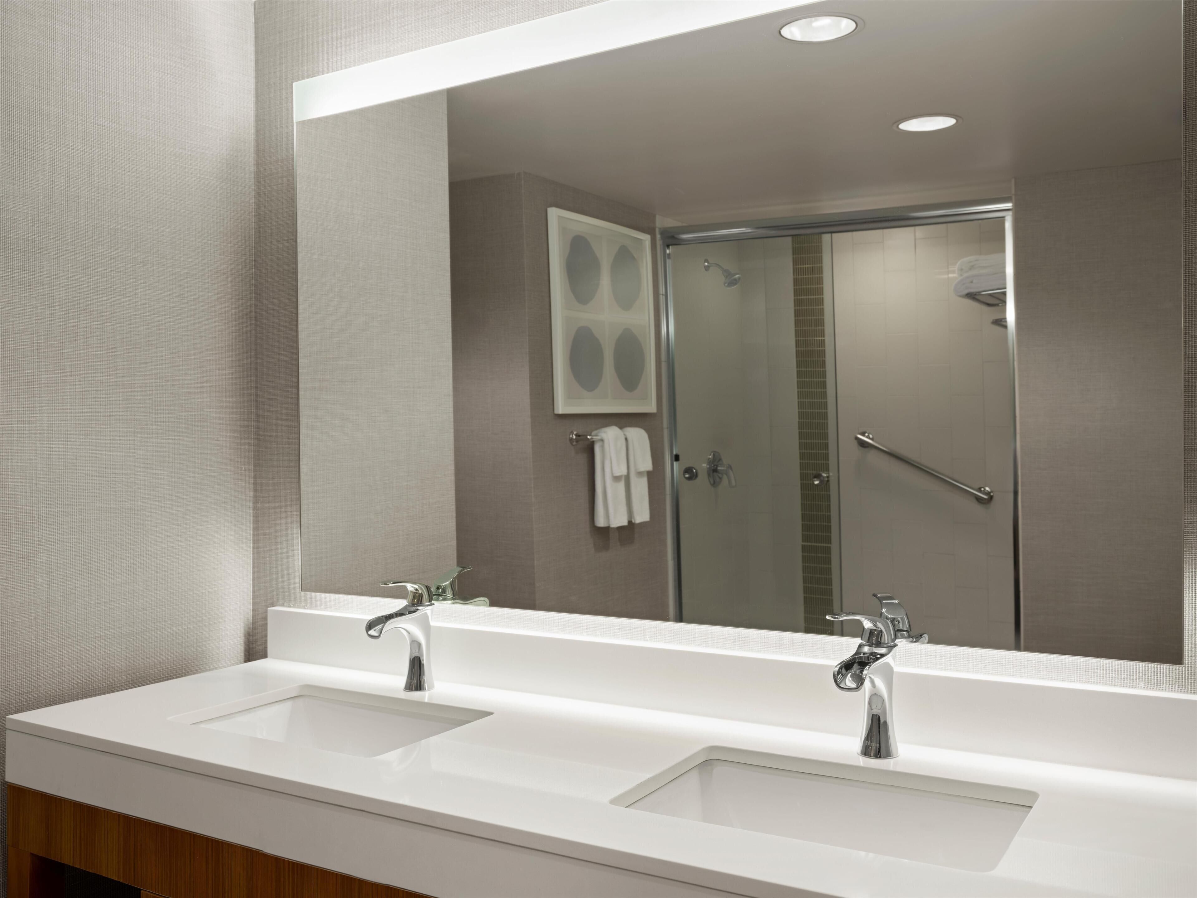 Une salle de bain moderne avec deux lavabos, un grand miroir et un espace douche.