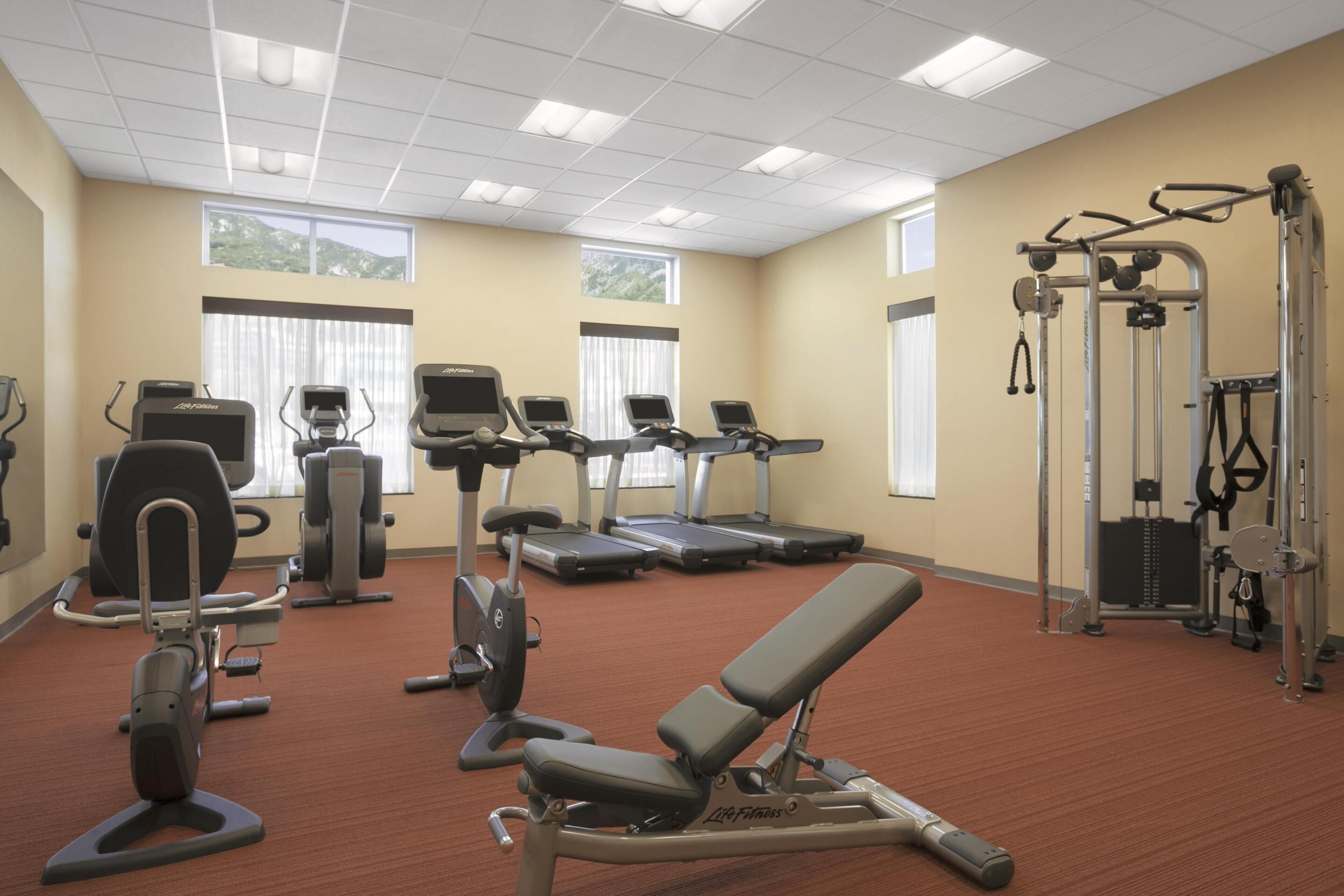 A gym with treadmills, elliptical machines, weight machines, and a bench.
