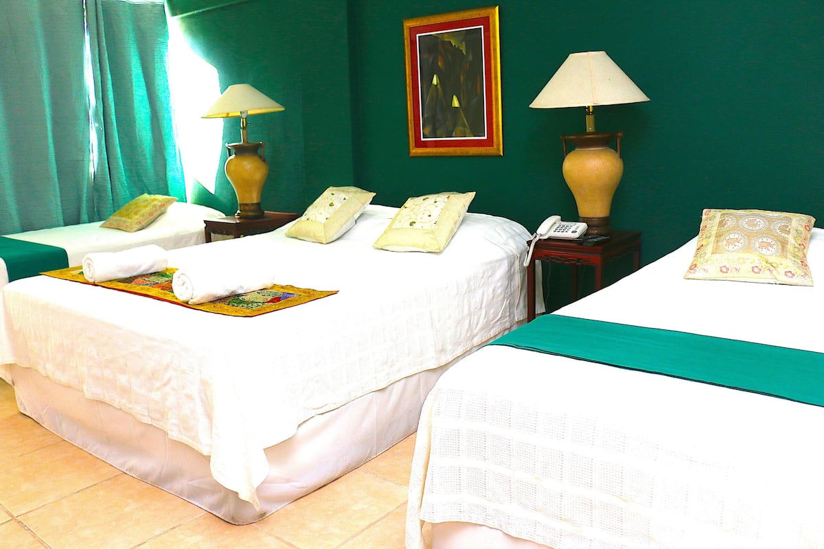 A hotel room with two beds, each with a white bedspread, two bedside lamps, a telephone, and a painting on the wall.