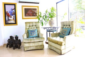 Een woonkamer met twee fauteuils, een vaas met een plant en twee ingelijste kunstwerken aan de muur.