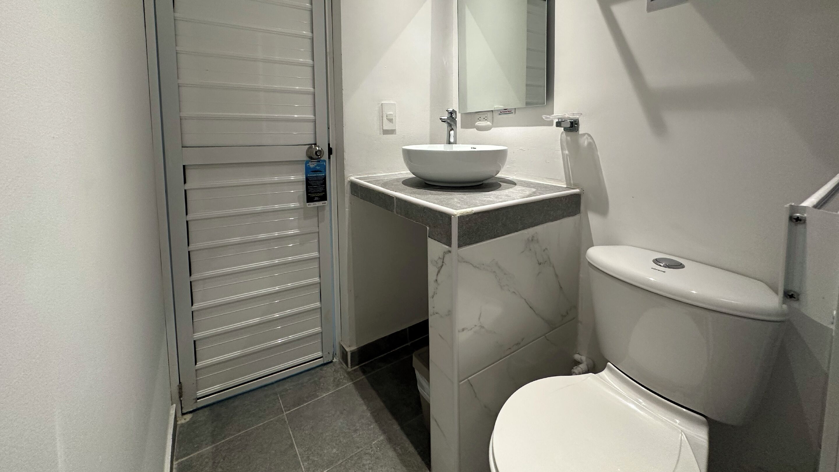 A modern bathroom with a white toilet, a marble sink, and a mirror above it.