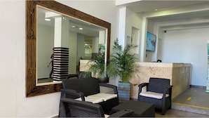 A lobby with a reception desk, two wicker chairs, a large mirror, and a potted plant. - Hotel Tower by On vacation (San Andrés)