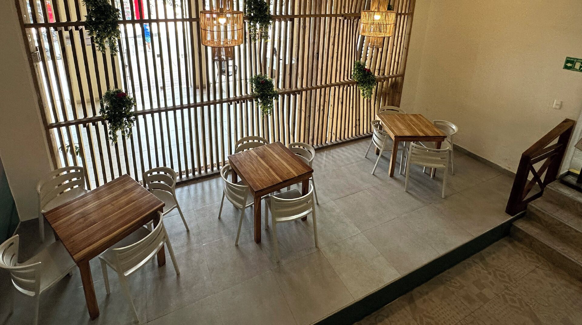 A restaurant interior with wooden tables and chairs, a bamboo partition, and hanging lights.