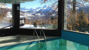 An indoor swimming pool with metal ladders, a view of snow-capped mountains, and a clear sky. - Baita della Luna (Cesana Torinese)
