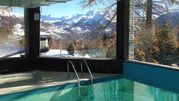 An indoor swimming pool with metal ladders, a view of snow-capped mountains, and a clear sky. - Baita della Luna (Cesana Torinese)