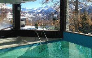Ein Hallenbad mit Metallleitern, Blick auf verschneite Berge und einem klaren Himmel.
