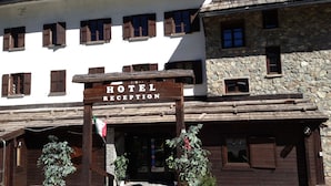 A hotel reception with a wooden sign, stone building, and wooden shutters. - Baita della Luna (Cesana Torinese)