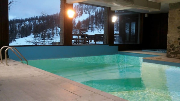 A swimming pool with a view of a snowy landscape and a wooden deck.