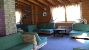 A cabin interior with wooden walls, a stone fireplace, and green upholstered seating. - Baita della Luna (Cesana Torinese)