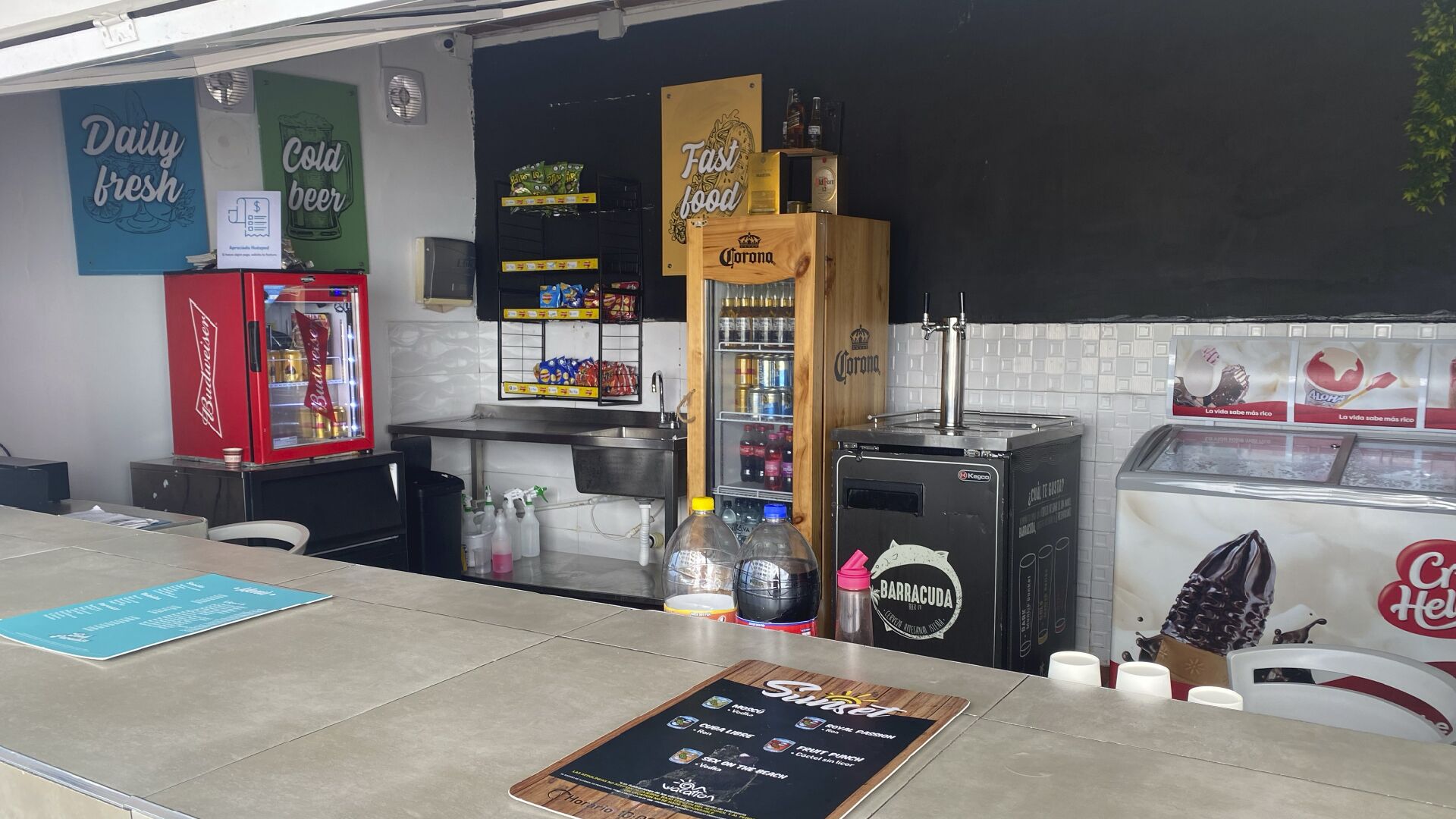 A bar area with a Budweiser refrigerator, Corona beer tap, and a Barracuda beer tap. There are also various snacks and condiments on the counter.