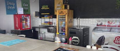 A bar area with a Budweiser refrigerator, Corona beer tap, and a Barracuda beer tap. There are also various snacks and condiments on the counter.