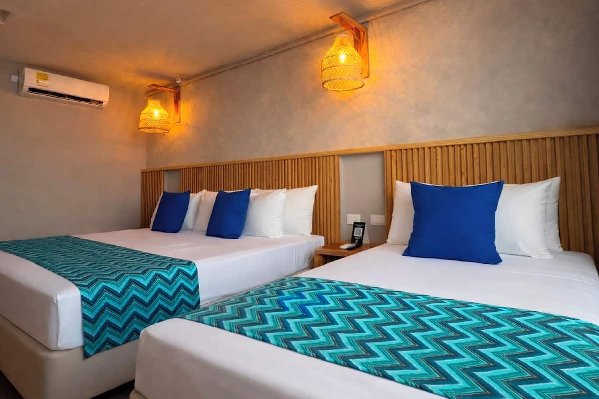A hotel room with two beds, each with a patterned bedspread, wooden headboards, and wall-mounted lamps.