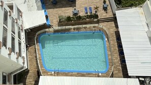 Piscina no terraço com deck de madeira, rodeada por espreguiçadeiras e um pequeno jardim.