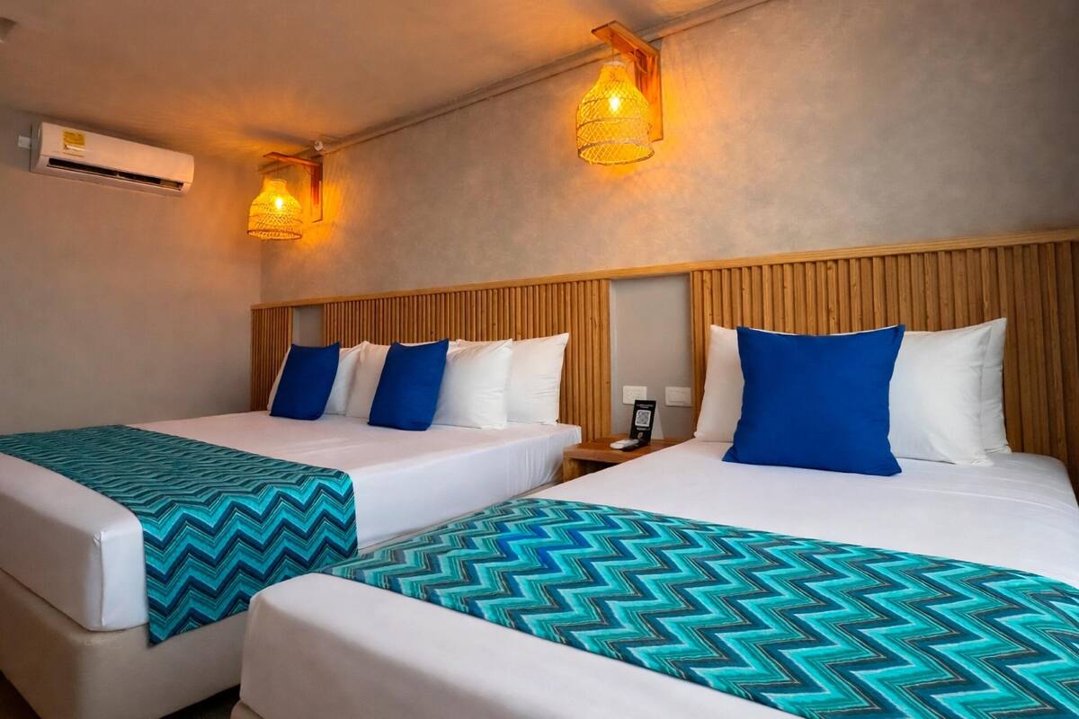 A hotel room with two beds, each with a patterned bedspread, a wooden headboard, and wall-mounted lights.
