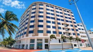 A multi-story hotel with a modern design, featuring a curved facade and a pool area with palm trees.