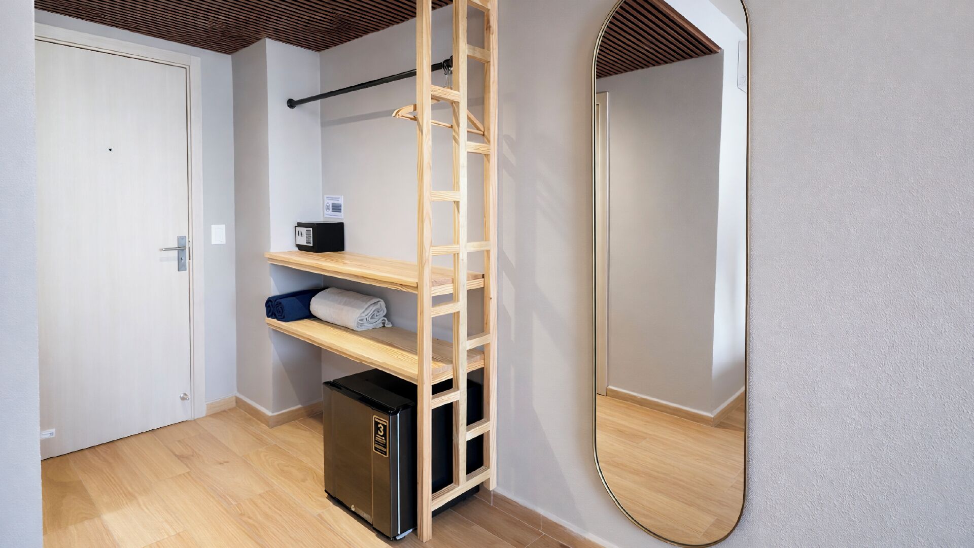 A compact room with a wooden ladder shelf, a small trash bin, a mirror, and a door.