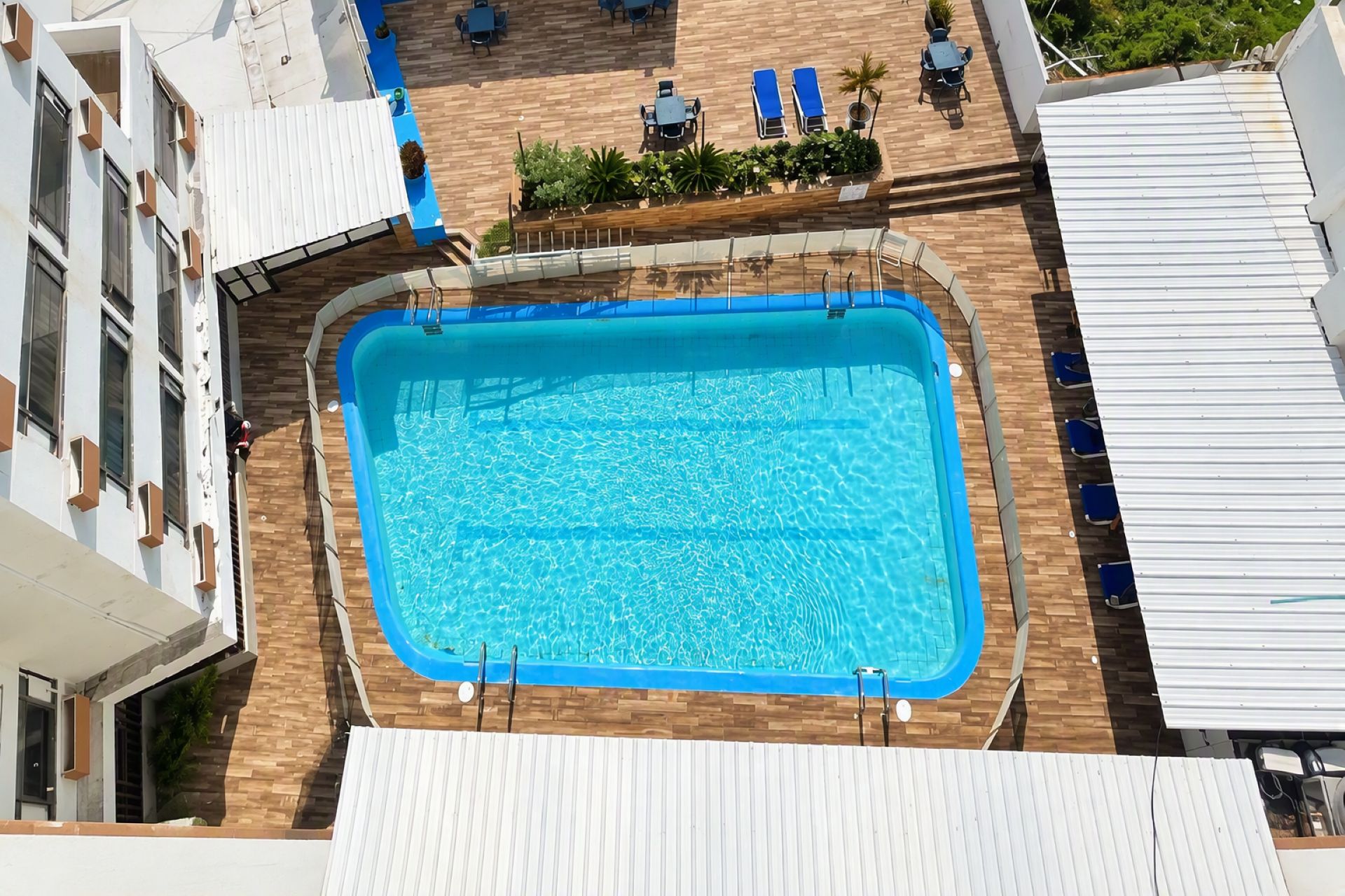 A rooftop swimming pool with a wooden deck, surrounded by lounge chairs and a small garden area.