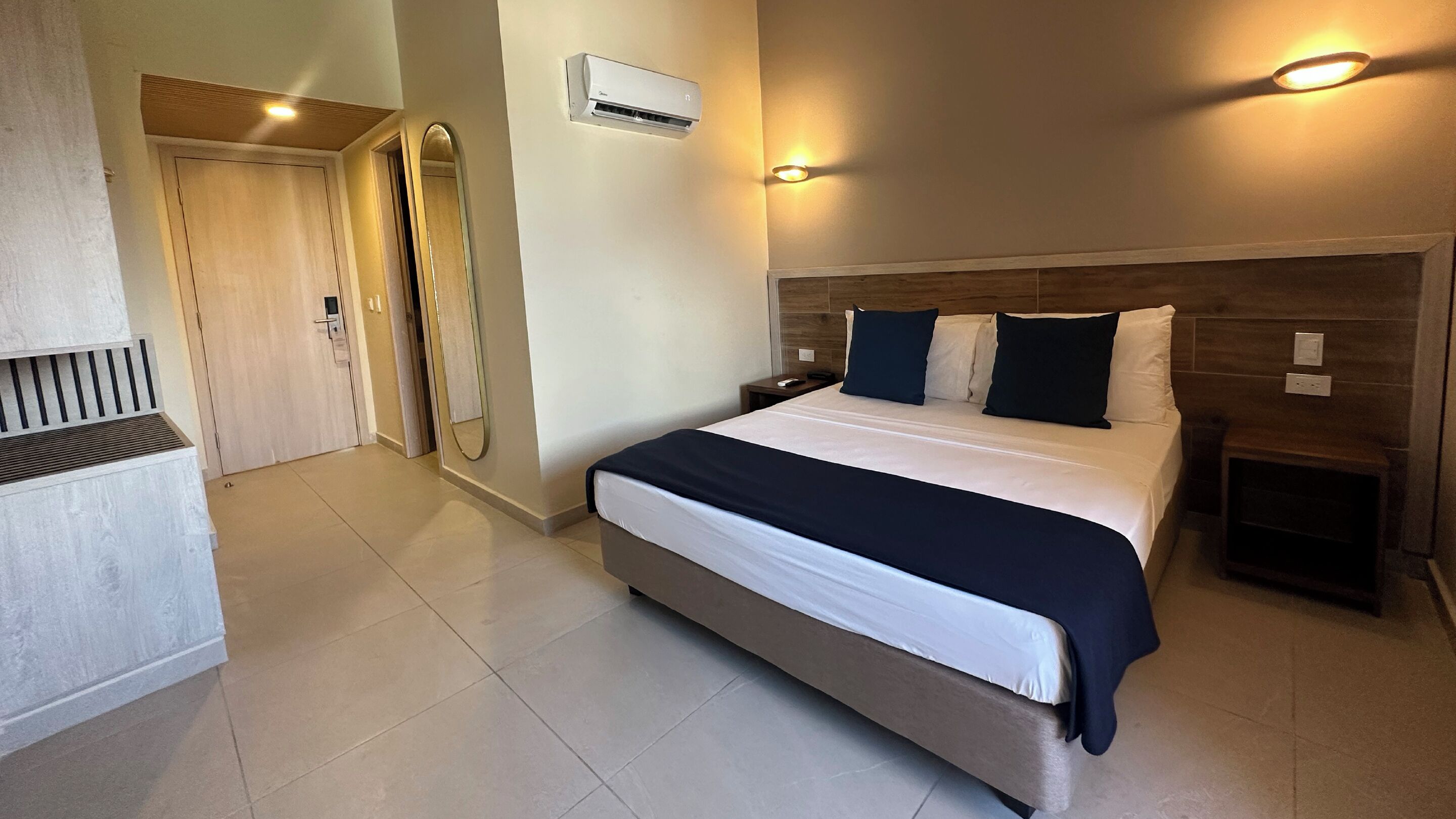 Een moderne hotelkamer met een groot bed, nachtkastjes, een spiegel en een airconditioning.