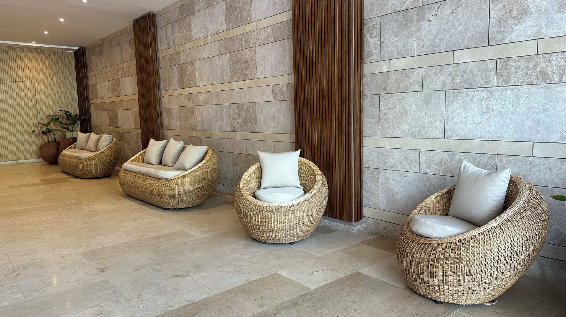 Un vestíbulo moderno con tres sillones de mimbre con cojines blancos, una columna de madera y una pared de piedra.