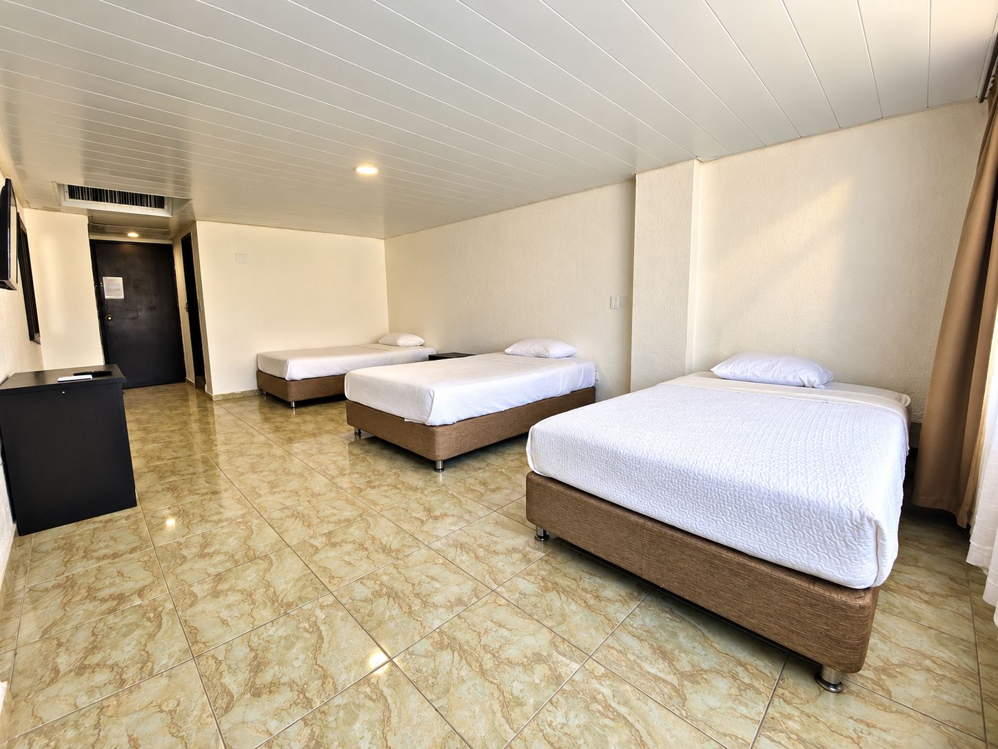 A hotel room with three single beds, a desk, and a tiled floor.