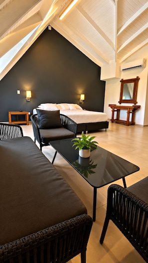 A modern bedroom with a sloped ceiling, a bed with white linens, a small table with a plant, and a wooden nightstand. - Hotel Lord Pierre (San Andrés)