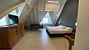 Una habitación con techo inclinado, una cama, un armario de madera, un escritorio y una silla.