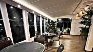 Un comedor interior con mesas y sillas redondas, ventanas amplias y suelo de madera.