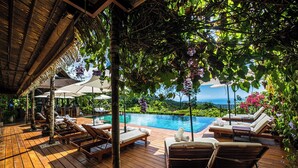 Une terrasse en bois avec des chaises longues et des parasols, donnant sur une piscine.