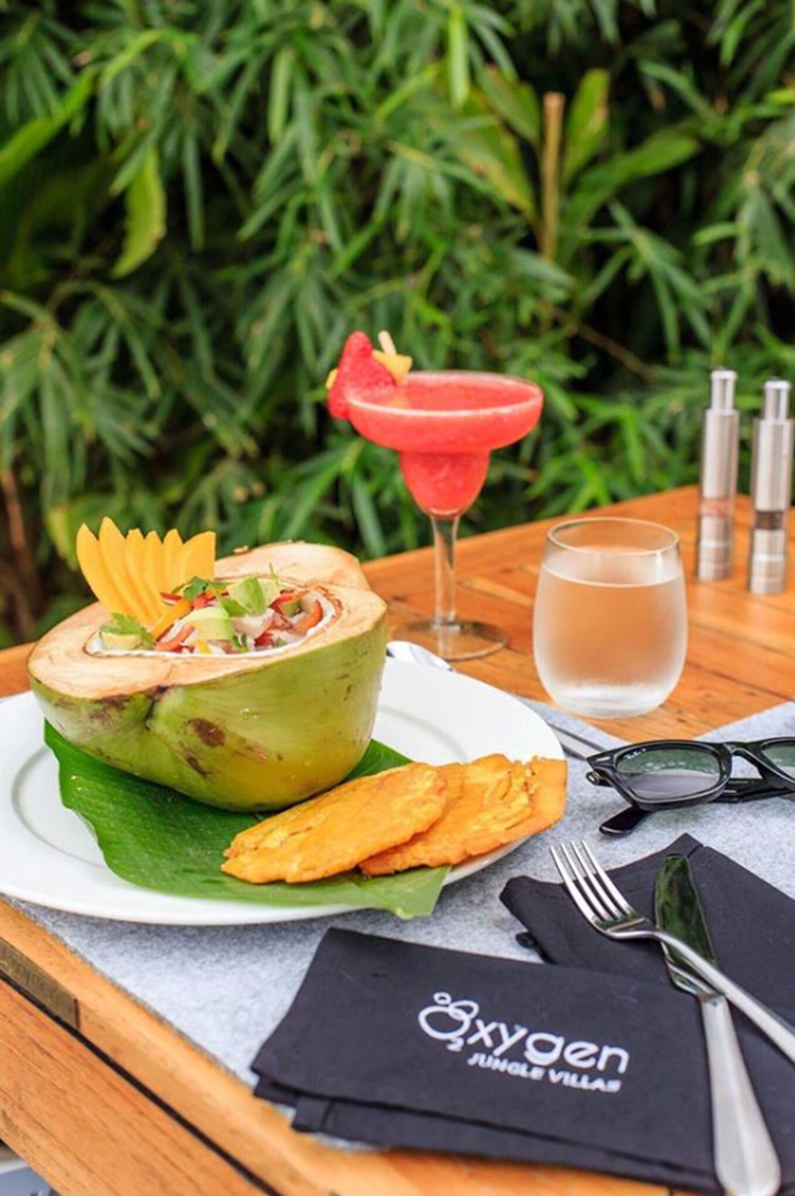 A table with a dish on a banana leaf, a cocktail, and a glass of water.