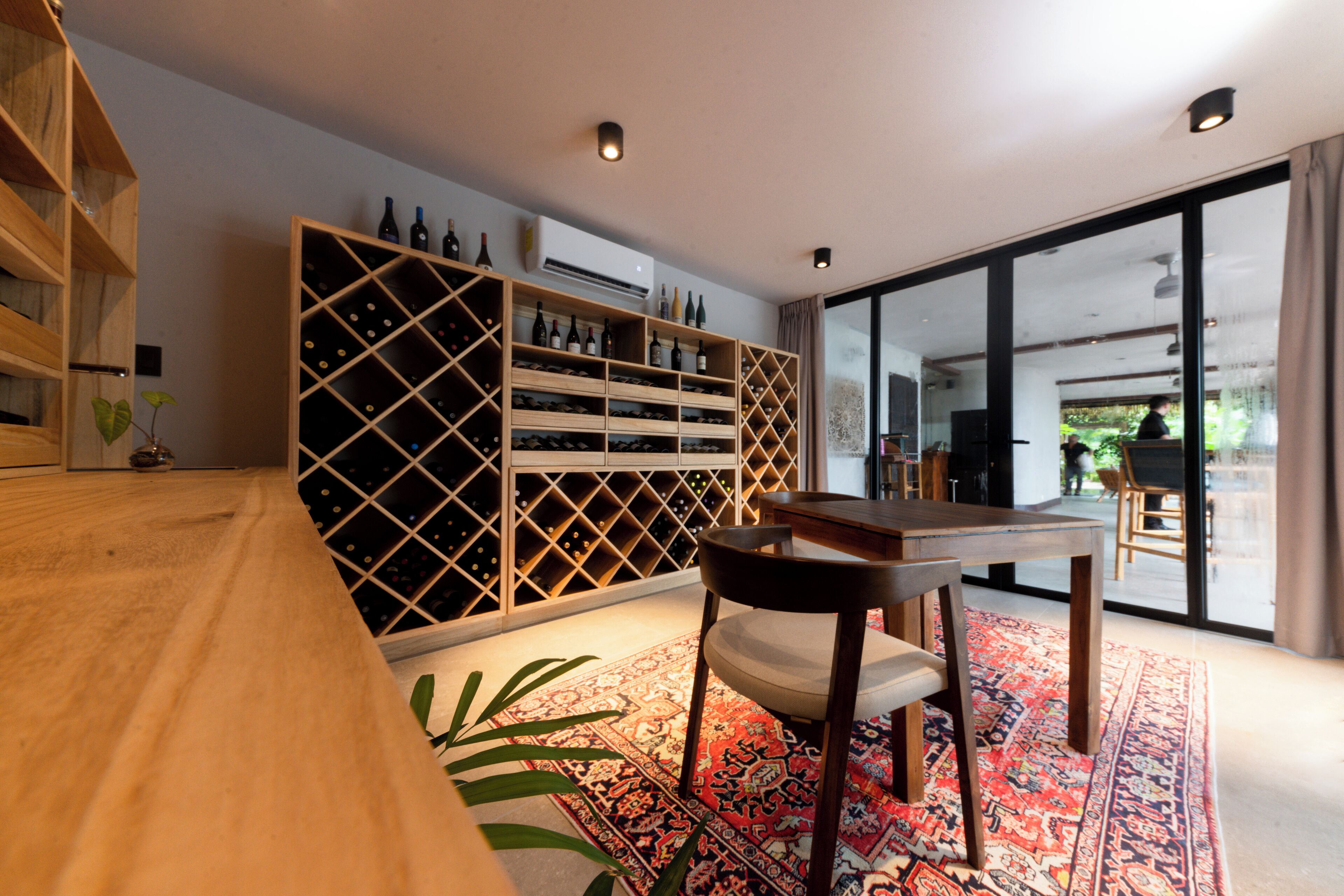 A modern interior with a wooden table and chairs, a wine rack, and a large glass door leading to an outdoor area.