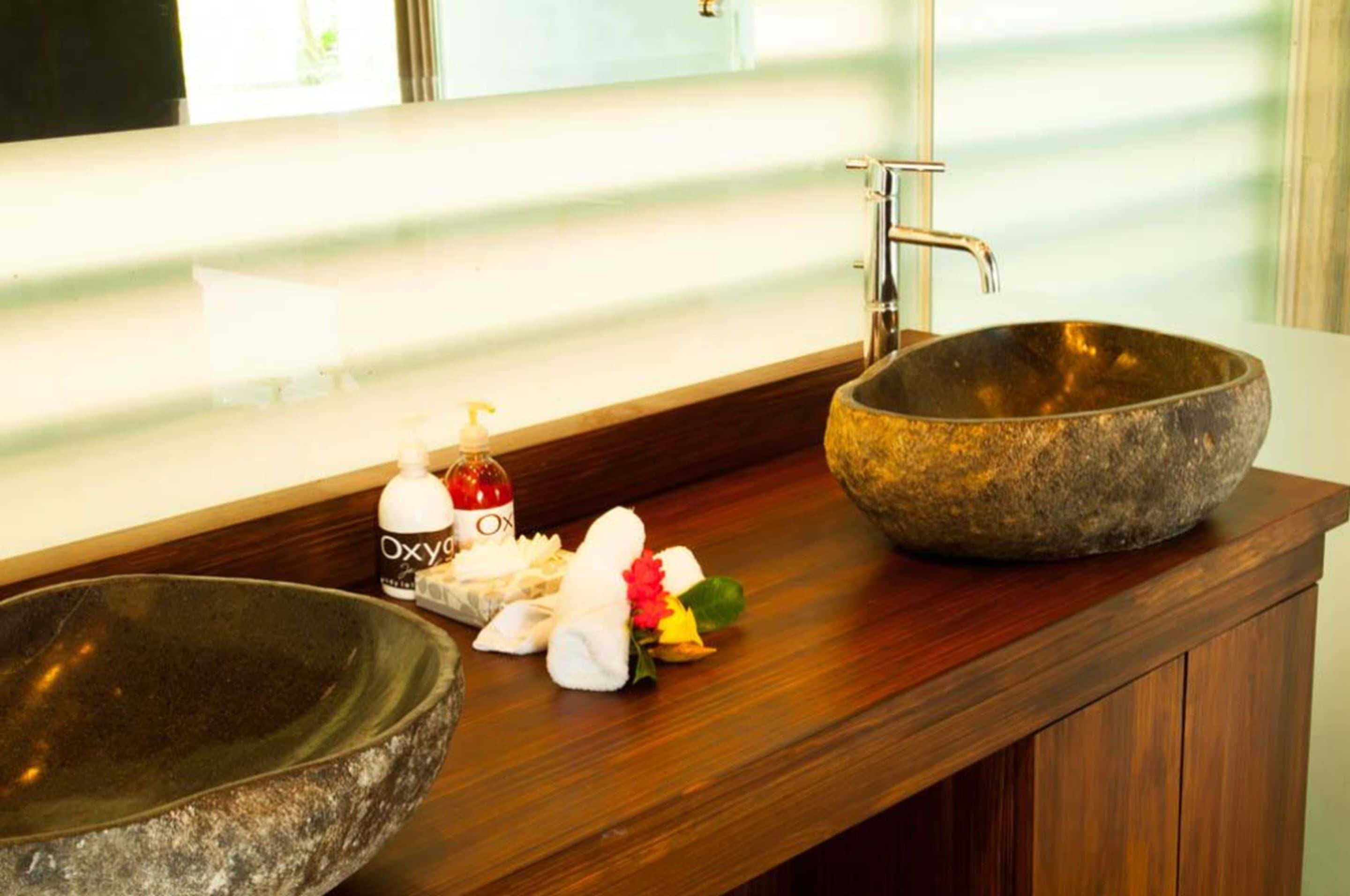 A bathroom with a wooden vanity, a stone sink, a faucet, and toiletries.