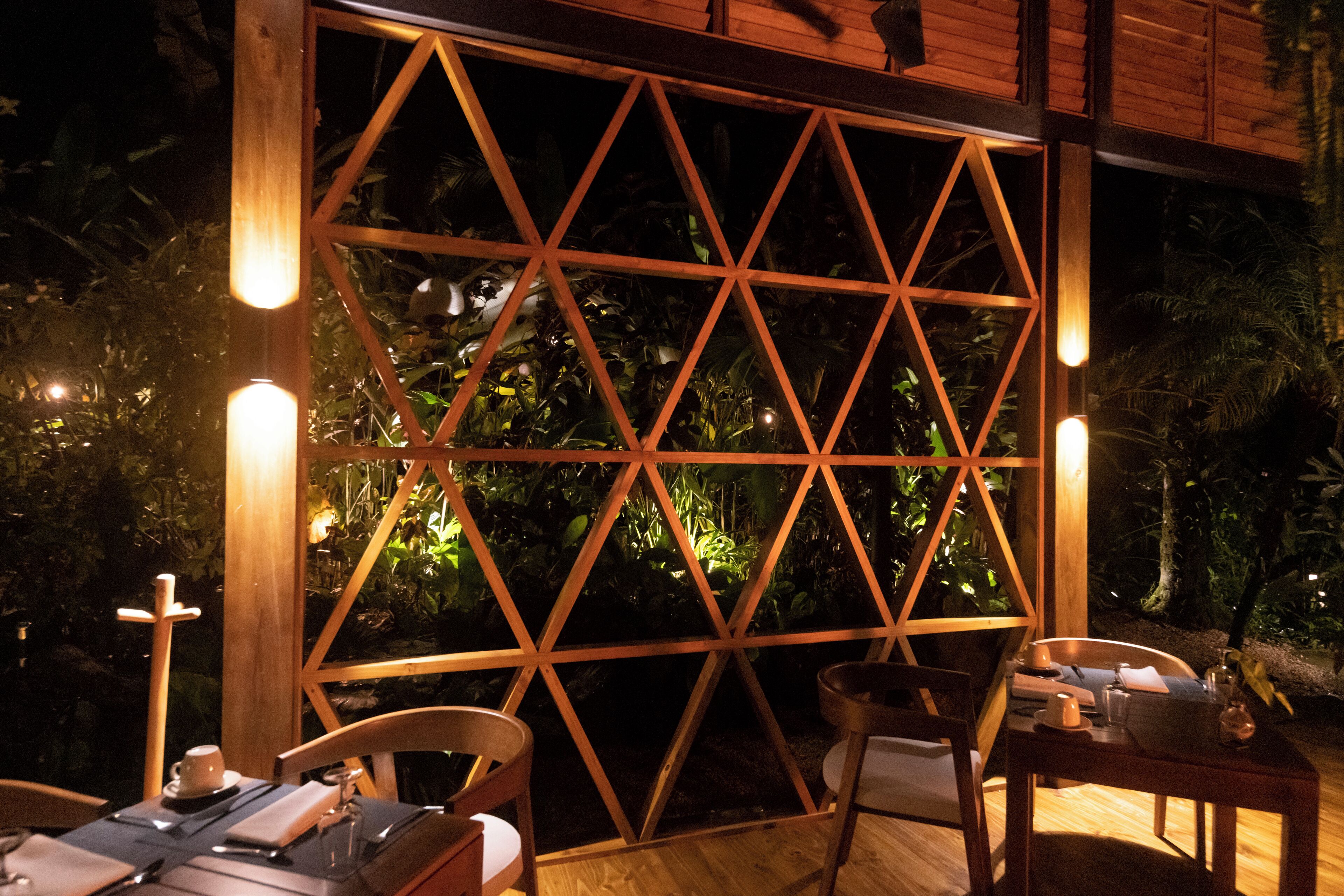 An outdoor dining area with a wooden lattice partition, chairs, and tables set up for dining.